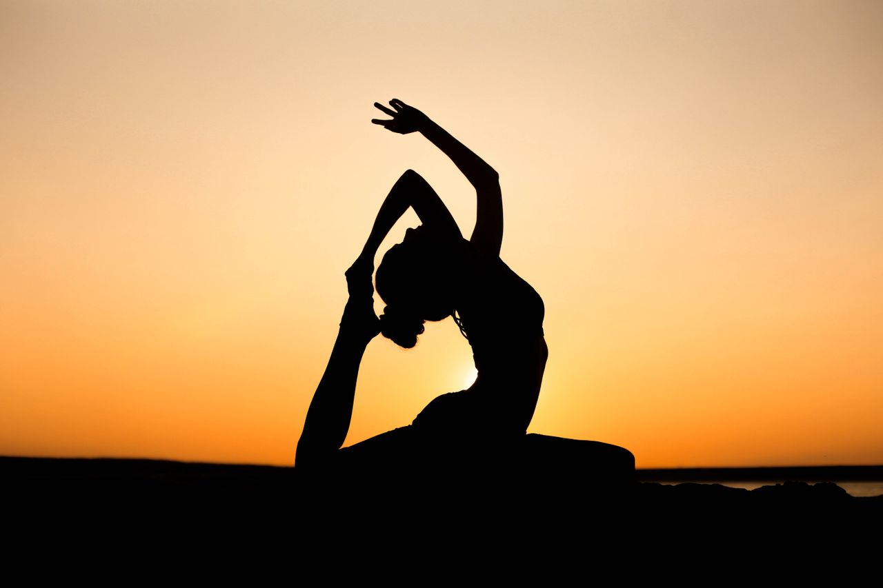 Home A woman in a yoga pose silhouetted against a vibrant sunset sky, embodying peace and wellness.