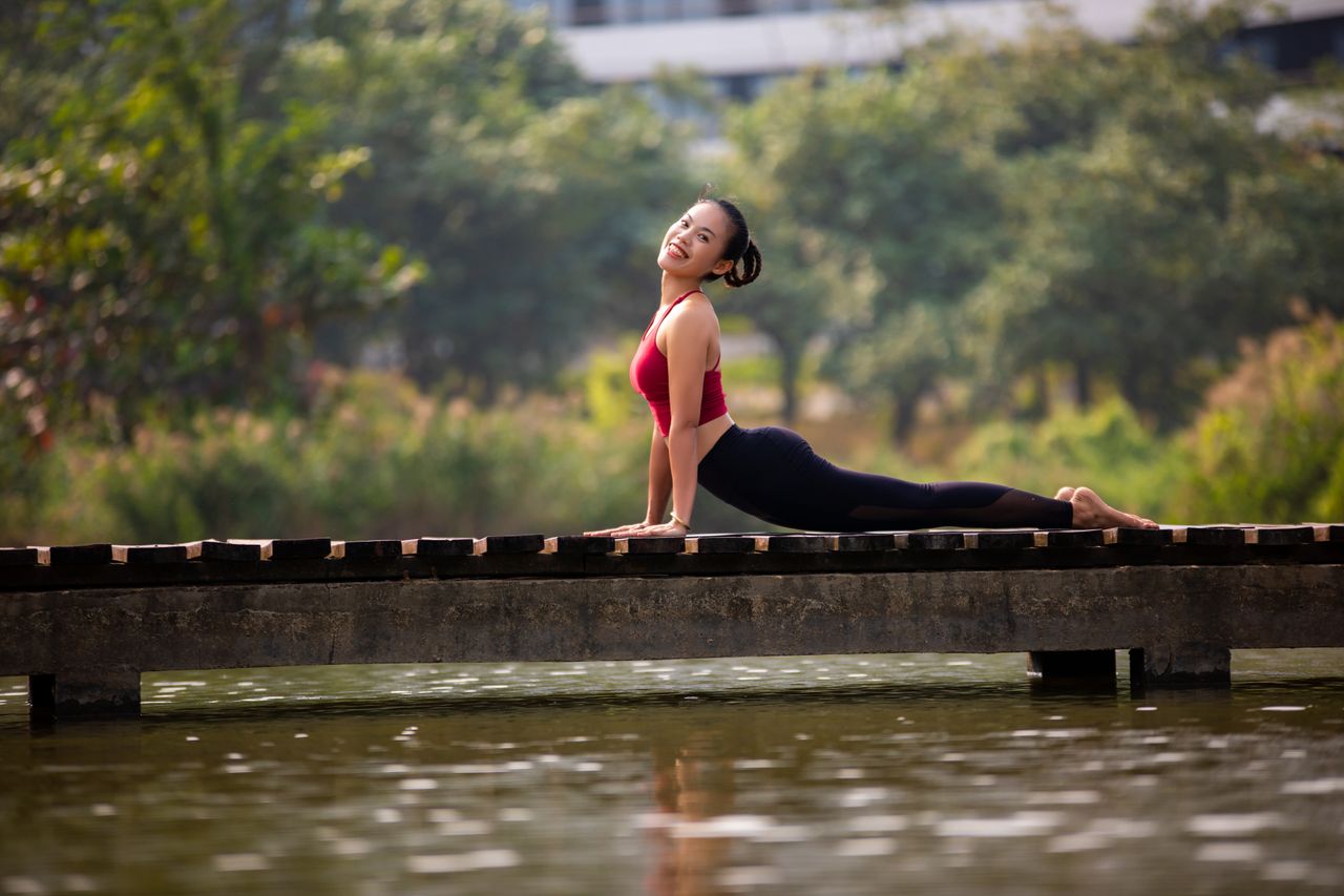 about-01 A woman enjoys a yoga pose on a bridge, showcasing flexibility and relaxation in a natural setting.