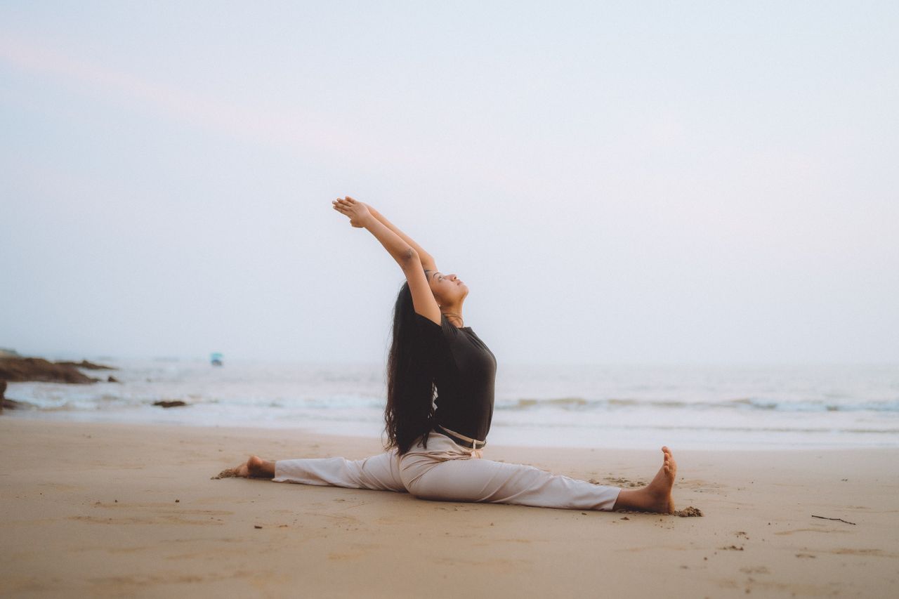Home Serene beach yoga session at sunrise with woman performing splits, embodying calm and balance.