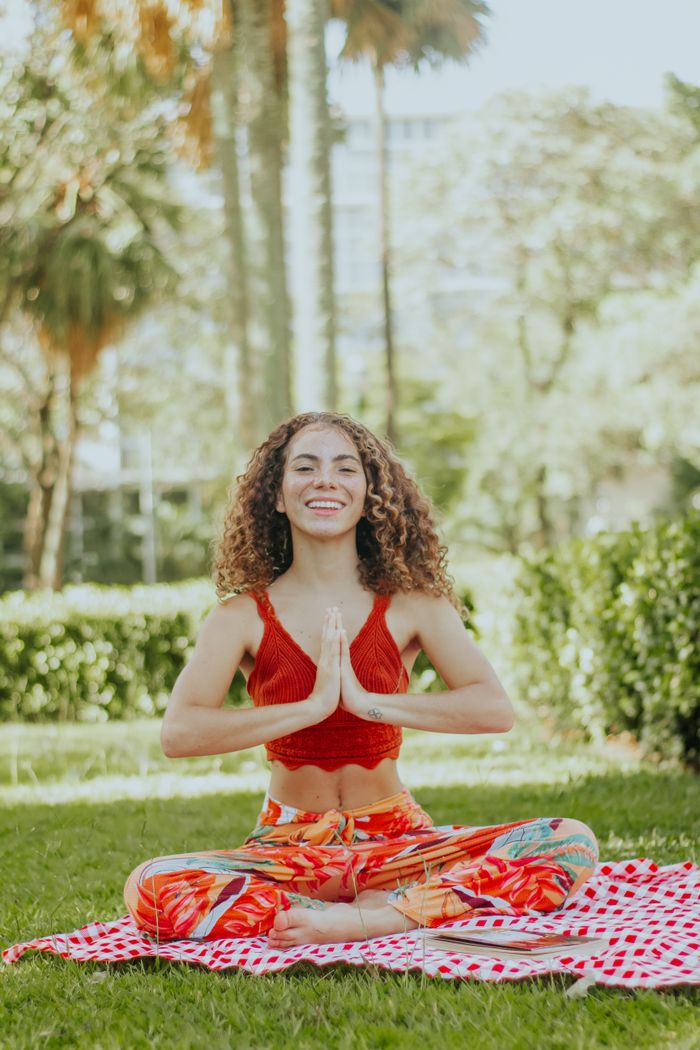 project-01-c Smiling woman meditating on a mat in a sunny park, exuding calm and relaxation.